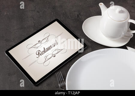 Tablet with stylish restaurant logo and laid table  Stock Photo