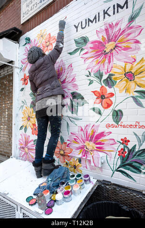 The muralist  @surfaceofbeauty painting a floral work in progress on the Lower East Side of Manhattan, New York City. Stock Photo