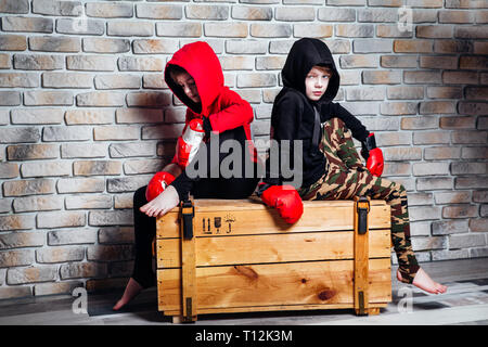 Little twin brothers dressing in sportswear wearing boxing gloves posing in a studio. Stock Photo