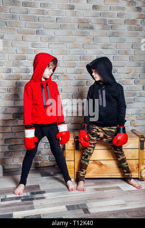 Little twin brothers dressing in sportswear wearing boxing gloves posing in a studio. Stock Photo