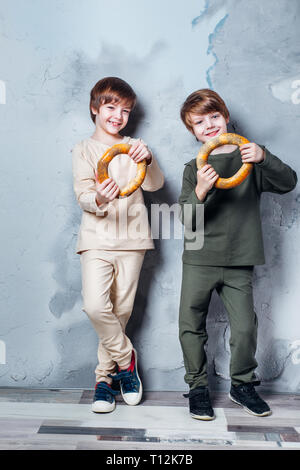Little twin boys playing and dreaming of becoming a spaceman. Portrait of funny kids with bagels on gray wall Stock Photo