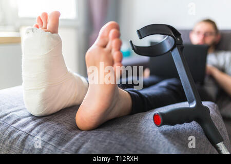 man with a sprained ankle sitting on a sofa at home Stock Photo
