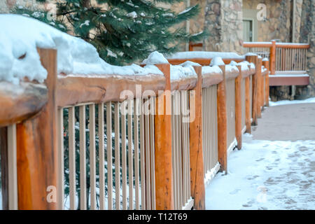Building railing topped with snow in Park City. Rustic wooden railing of a balcony in Park City, Utah topped with snow in winter. A tree and building  Stock Photo