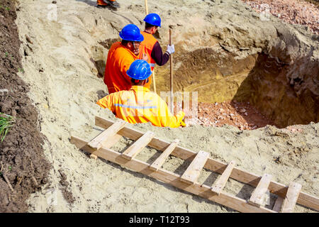 Construction workers are using shovels to realign level of gravel in square base trench. Stock Photo
