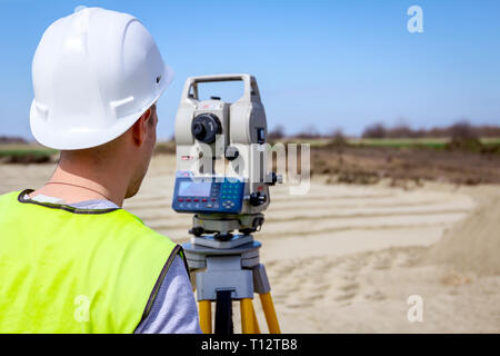 Surveyor engineer is measuring level on construction site. Surveyors ensure precise measurements before undertaking large construction projects. Stock Photo