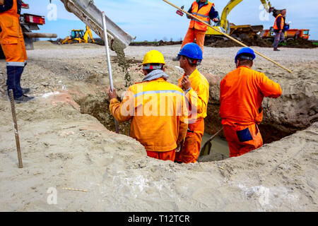 Workers are spreading fresh concrete in square trench pouring from mixer truck. Stock Photo
