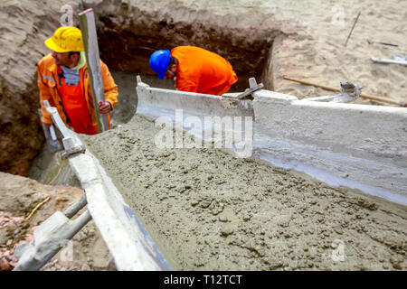 Workers are spreading fresh concrete in square trench pouring from mixer truck. Stock Photo