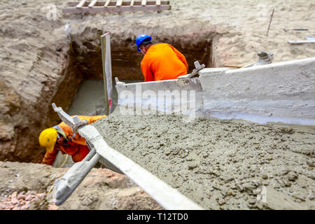 Workers are spreading fresh concrete in square trench pouring from mixer truck. Stock Photo