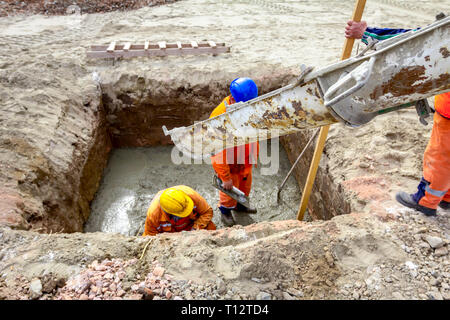 Workers are spreading fresh concrete in square trench pouring from mixer truck. Stock Photo