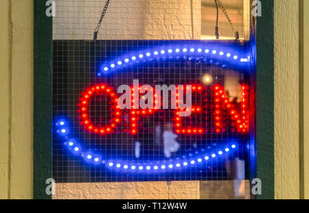 Neon Open sign on the door of an establishment. Close up of a red and blue neon Open sign hanging on the door of an establishment with screen mesh wir Stock Photo
