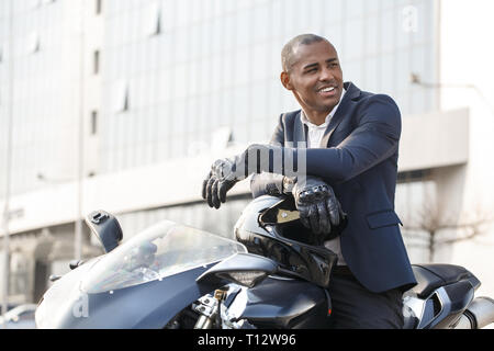 Young african american businessman sitting on motorcycle wearing sport gloves looking aside smiling happy Stock Photo