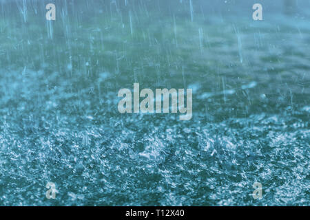 Droplets hitting water surface. Raindrops falling on the blue surface of water.  Motion blur. Stock Photo