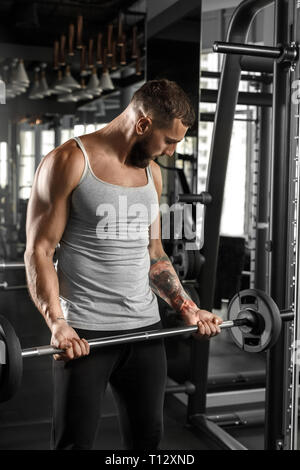Bodybuilding. Bearded man standing at gym lifting barbell looking at muscle tension Stock Photo