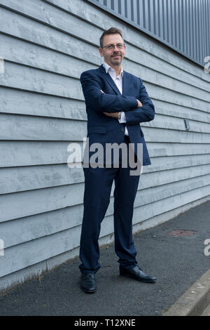 A businessman standing while wearing a suit and looking smart in a British suburban industrial estate on the outskirts of an English town Stock Photo