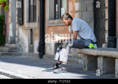Warsaw, Poland - August 22, 2018: Old town market square with worker museum employee man sitting on street bench during summer day closeup Stock Photo