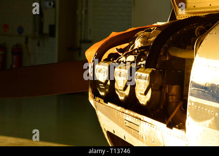 A small aircraft inside a maintenance hangar with its engine cover open, showing its Continental cylinder heads. Sunlight illuminates the aircraft. Stock Photo