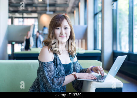 A female Asian student in a modern college campus poses for a photo. Stock Photo