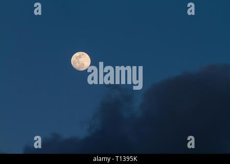 Full moon just risen in the dark blue sky with some gray clouds Stock Photo
