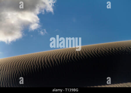 Shadow play on a sand dune with backlight effect and the sun shining in the blue sky with white one cloud Stock Photo