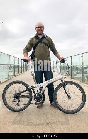 A white man stands on Shoreham's Adur Ferry Bridge with a folding bike Stock Photo