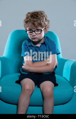 a board young white boy being restless and fed up on a colourful sofa Stock Photo