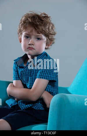 a board young white boy being restless and fed up on a colourful sofa Stock Photo