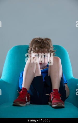 a board young white boy being restless and fed up on a colourful sofa Stock Photo