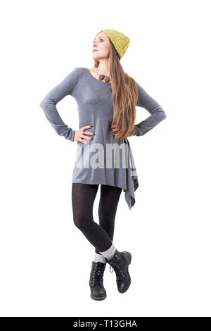 Young blonde woman in authentic fashion wearing yellow beanie cap and gray tunic looking up. Full body isolated on white background. Stock Photo