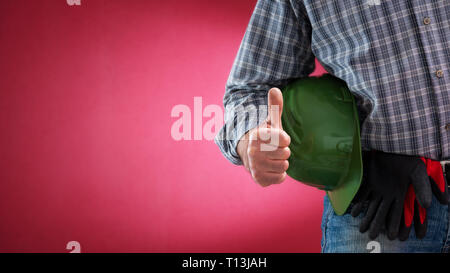 Caucasian construction worker in jeans and shirt, with helmet and protective gloves making ok sign with thumb up. Construction industry. Job security. Stock Photo