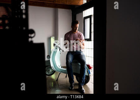 Man with motor scooter reading a book in a loft Stock Photo