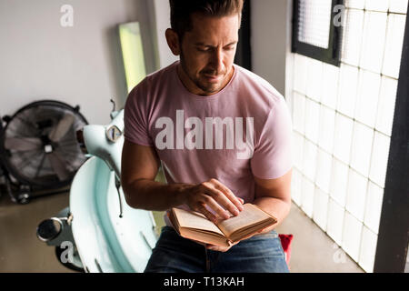 Man with motor scooter reading a book in a loft Stock Photo