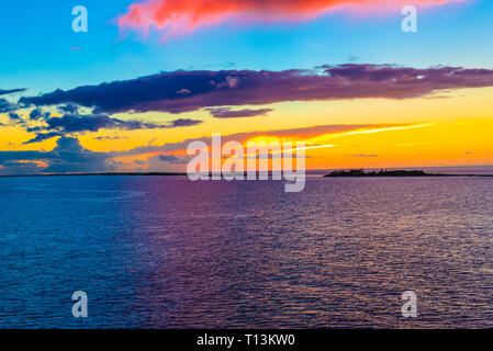 The sky turns orange and blue over  small islands in the Pacific Ocean at dusk. Stock Photo