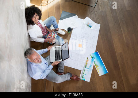Businessman and businesswoman sitting on the floor in a loft working with laptop and documents Stock Photo