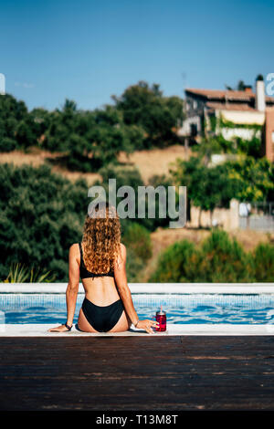 Pretty woman in a swimsuit sunbathing at the pool side, rear view Stock Photo