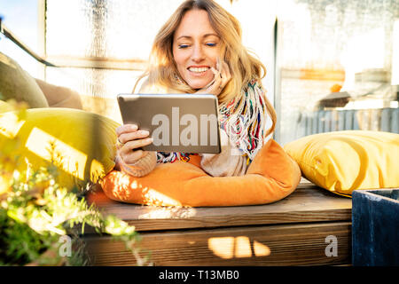 Portrait of smiling blond mature woman relaxing in winter garden using digital tablet Stock Photo