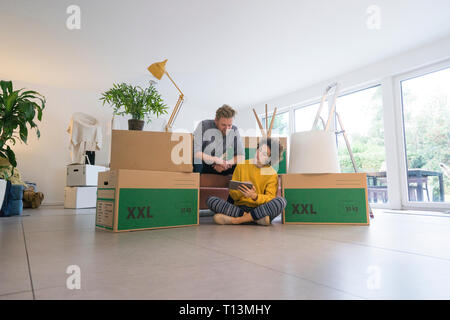 Couple sitting in living room with cardboard boxes using tablet Stock Photo