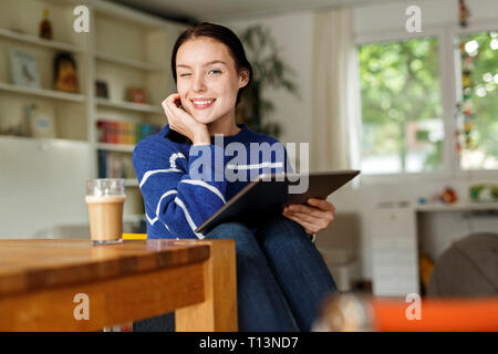 Young woman sitting at home, using digital tablet Stock Photo