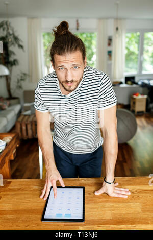 Young man with a bun standing at table, using digital tablet Stock Photo