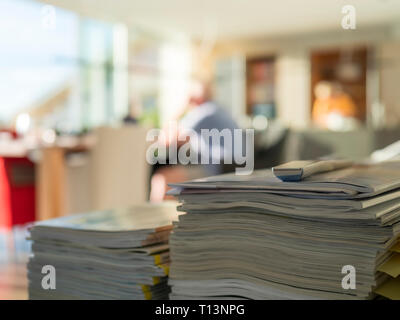 Stack of magazines in living room with man in background Stock Photo