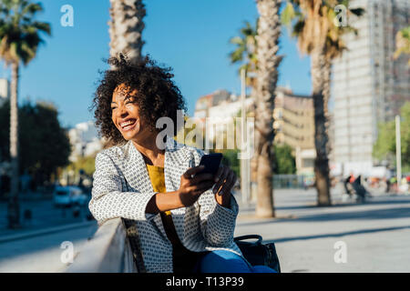 Beautiful woman sitting on a bench in the city, using smartphone Stock Photo