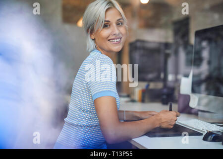 Young woman working in office, sitting at desk, smiling Stock Photo