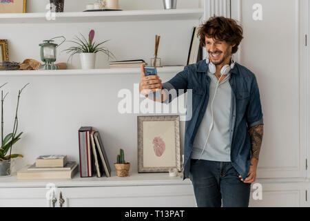 Man working standing in coworking space, using smartphone, with headphones around his neck Stock Photo