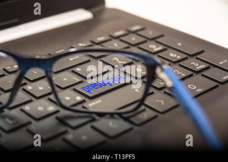 View of the PC keyboard through the lens of the glasses on the button with the written Presbyopia Stock Photo