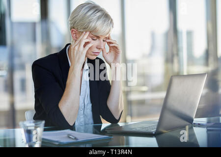 Exhausted businesswoman sitting at desk in office with closed eyes Stock Photo