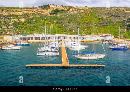 MGARR, GOZO, MALTA - FEBRUARY 02, 2013 - View of boats in the harbour with apartments on the hillside to the rear and people going about their busines Stock Photo