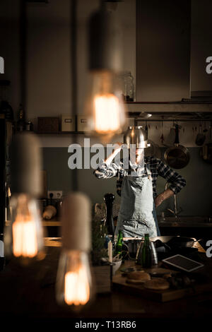 Man with apron standing in kitchen, wearing colander as helmet Stock Photo