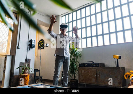 Mature man wearing VR glasses standing at the window in a loft Stock Photo