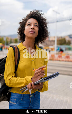 Portrait of woman with backpack, documents and pencil looking up Stock Photo