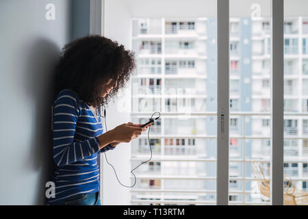 Young woman using smartphone and earphones at home Stock Photo