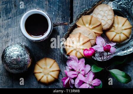 tasty coffee in a traditional Turkish cup and butter cookies and a sprig of pink flowers on a wooden table - flat lay food background Stock Photo